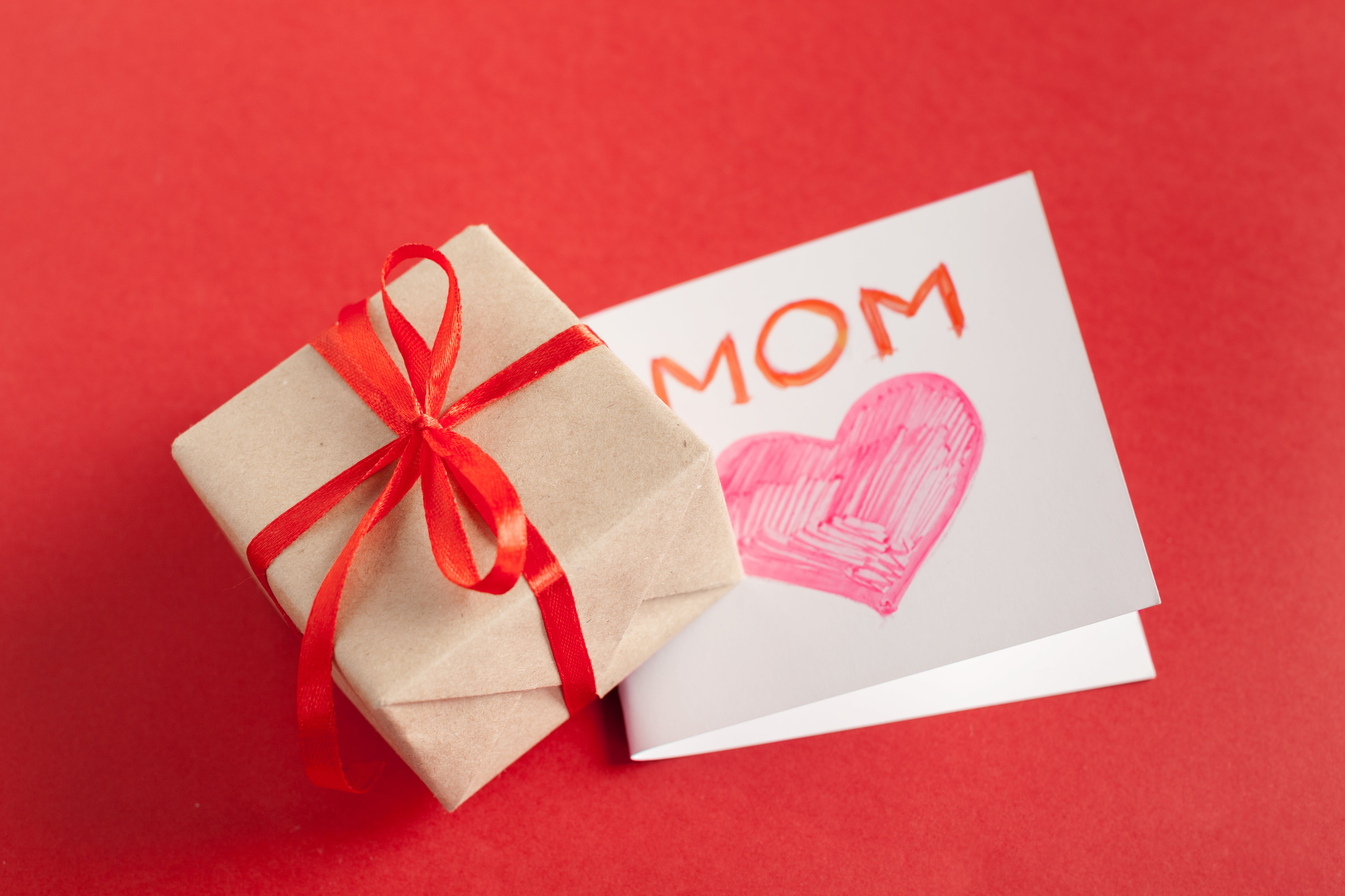 Mother’s Day gift box with red ribbon next to a “MOM” card on a red background