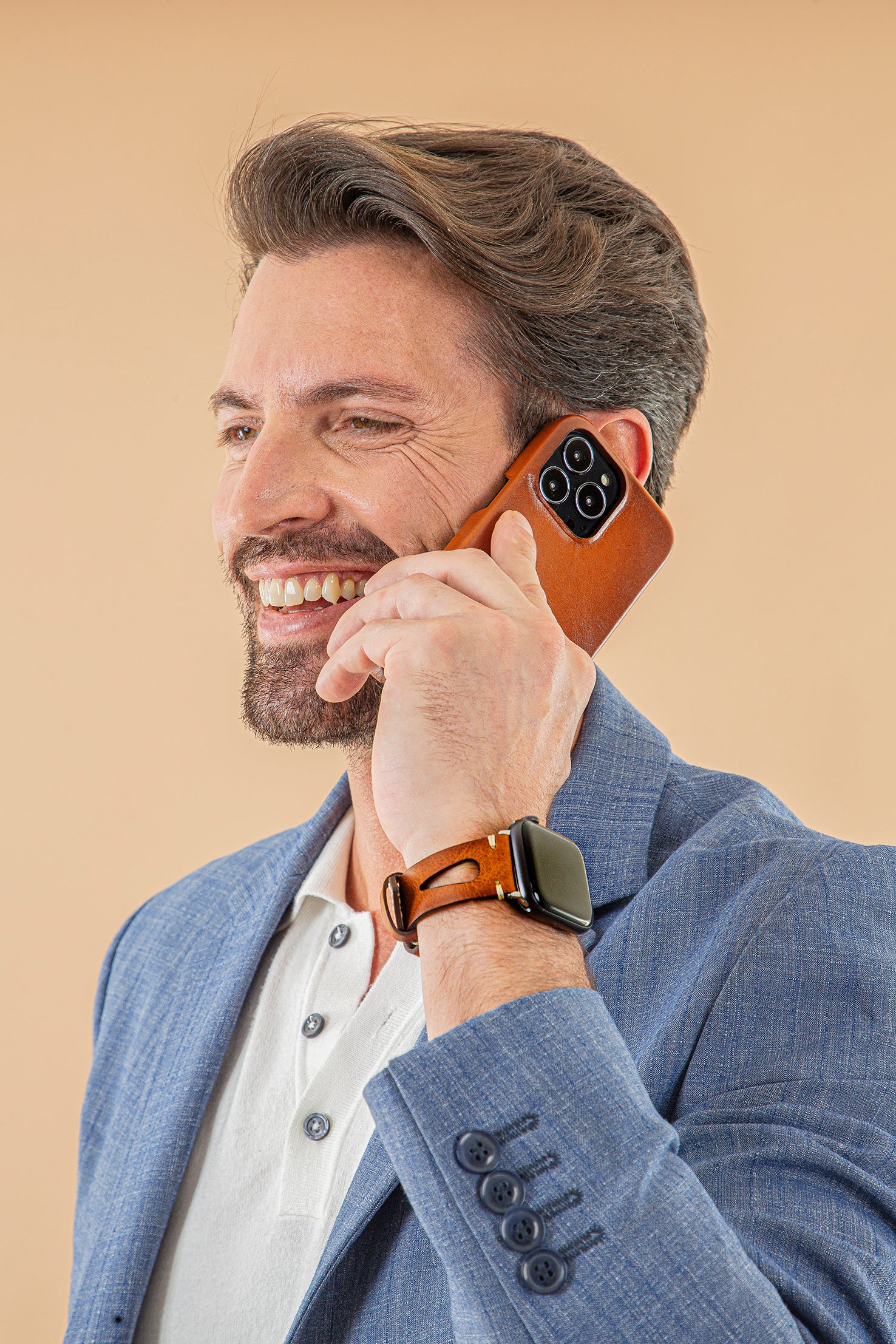 A man smiling while talking on an Apple Watch with a brown genuine leather band.