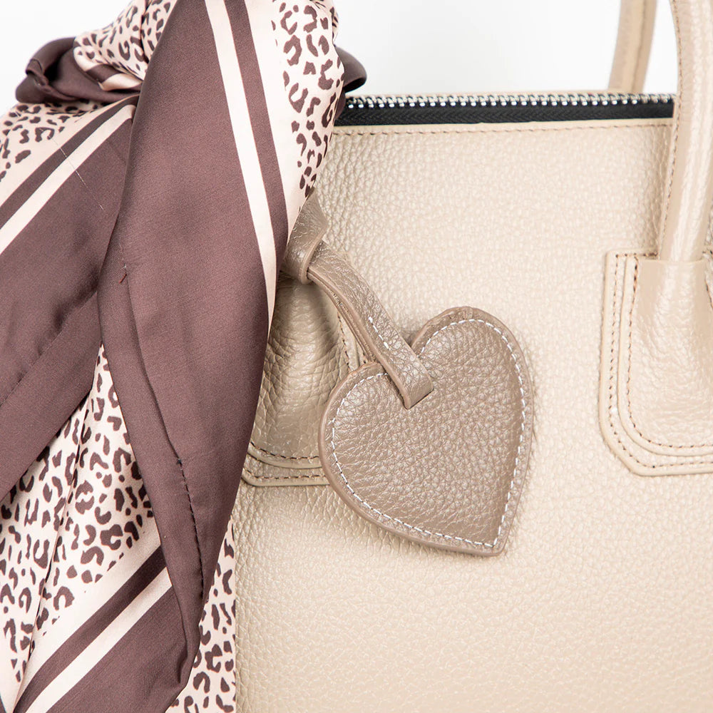 Beige handbag with a heart-shaped tag and a patterned scarf draped over it.