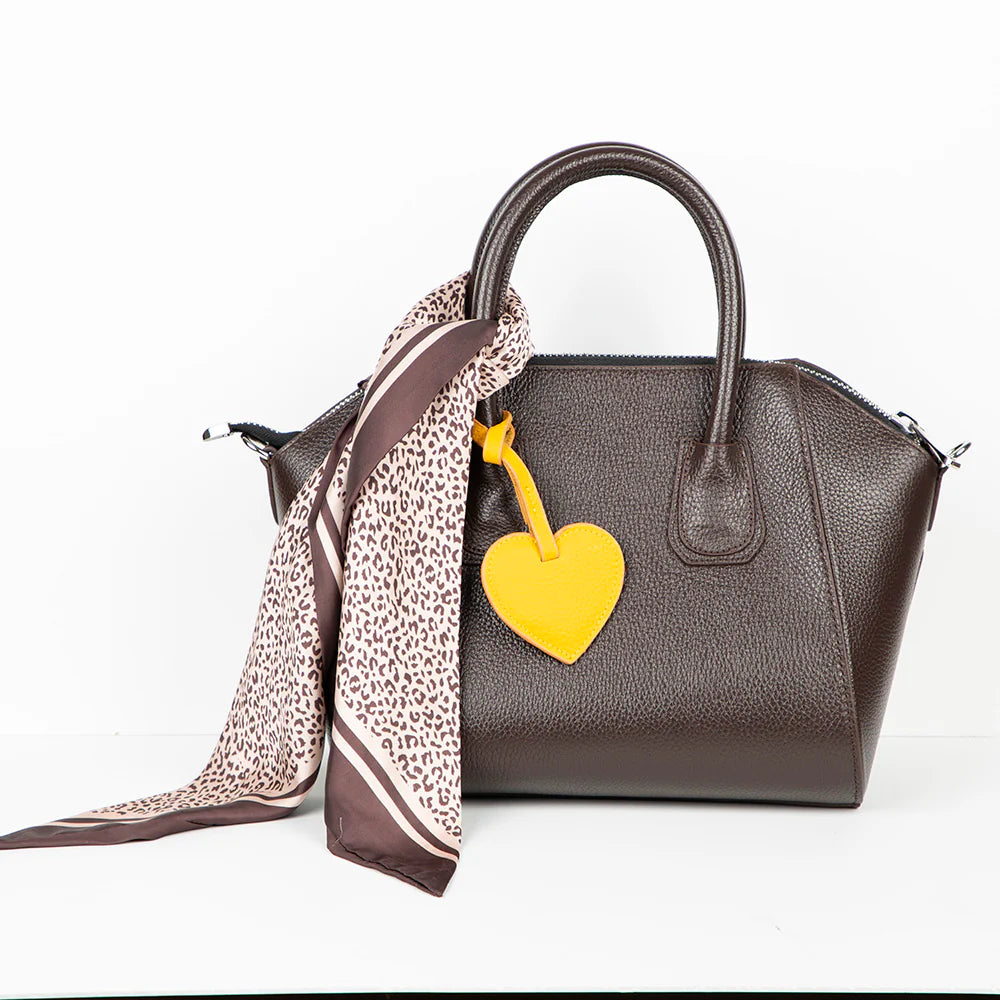 Brown handbag with a yellow heart charm and leopard print scarf on a white background