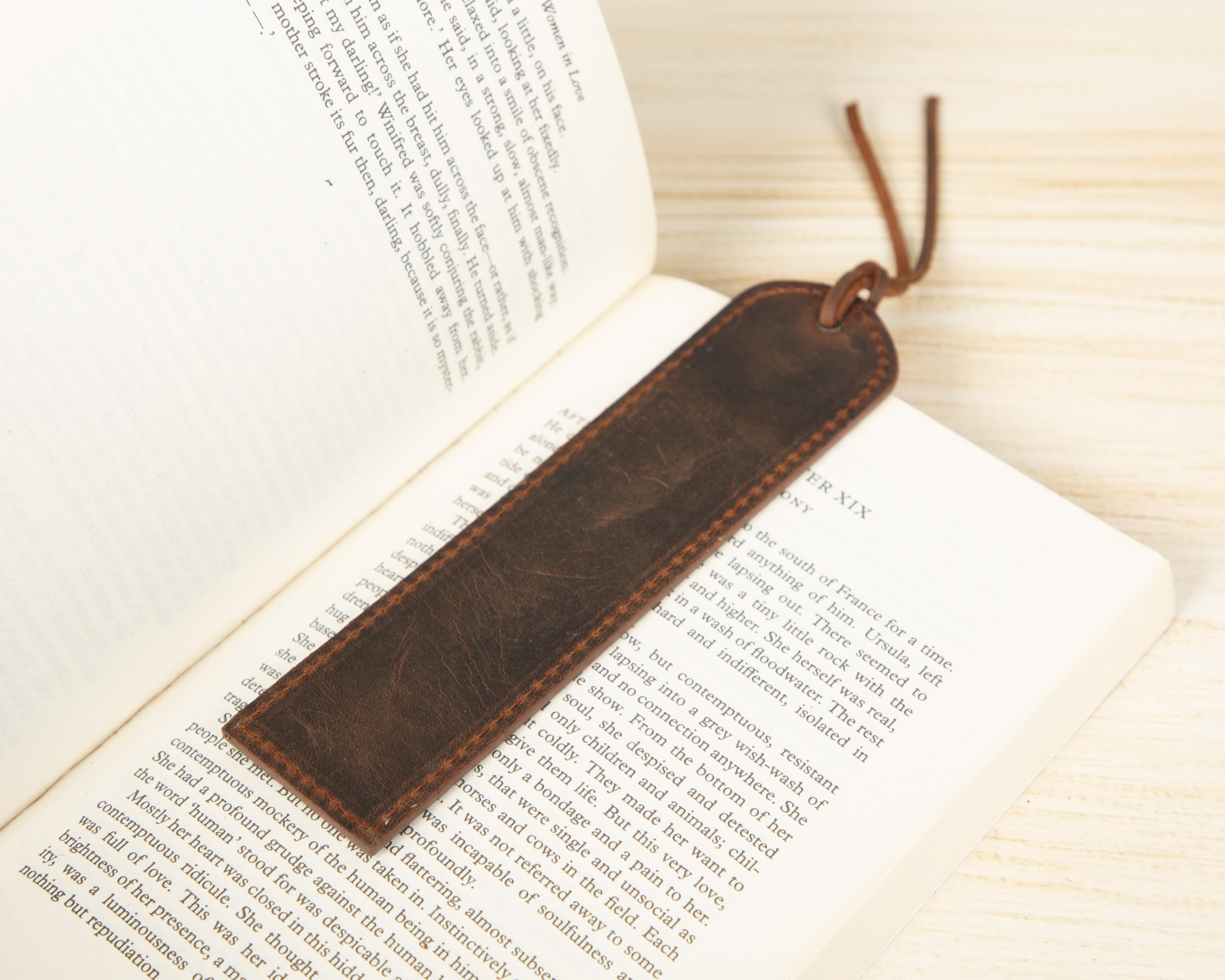Brown leather bookmark on an open book with a wooden surface underneath