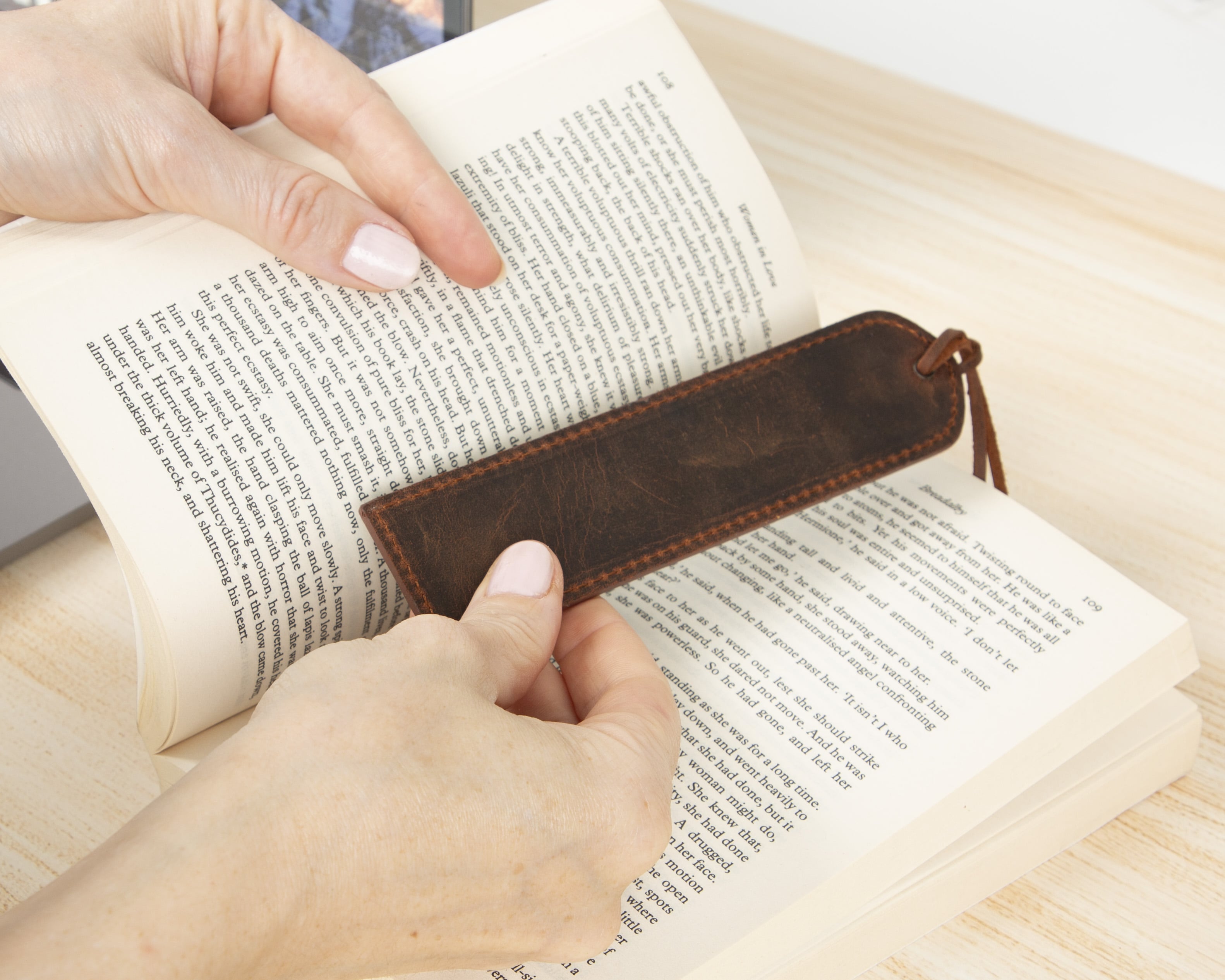 Person holding a leather bookmark on an open book