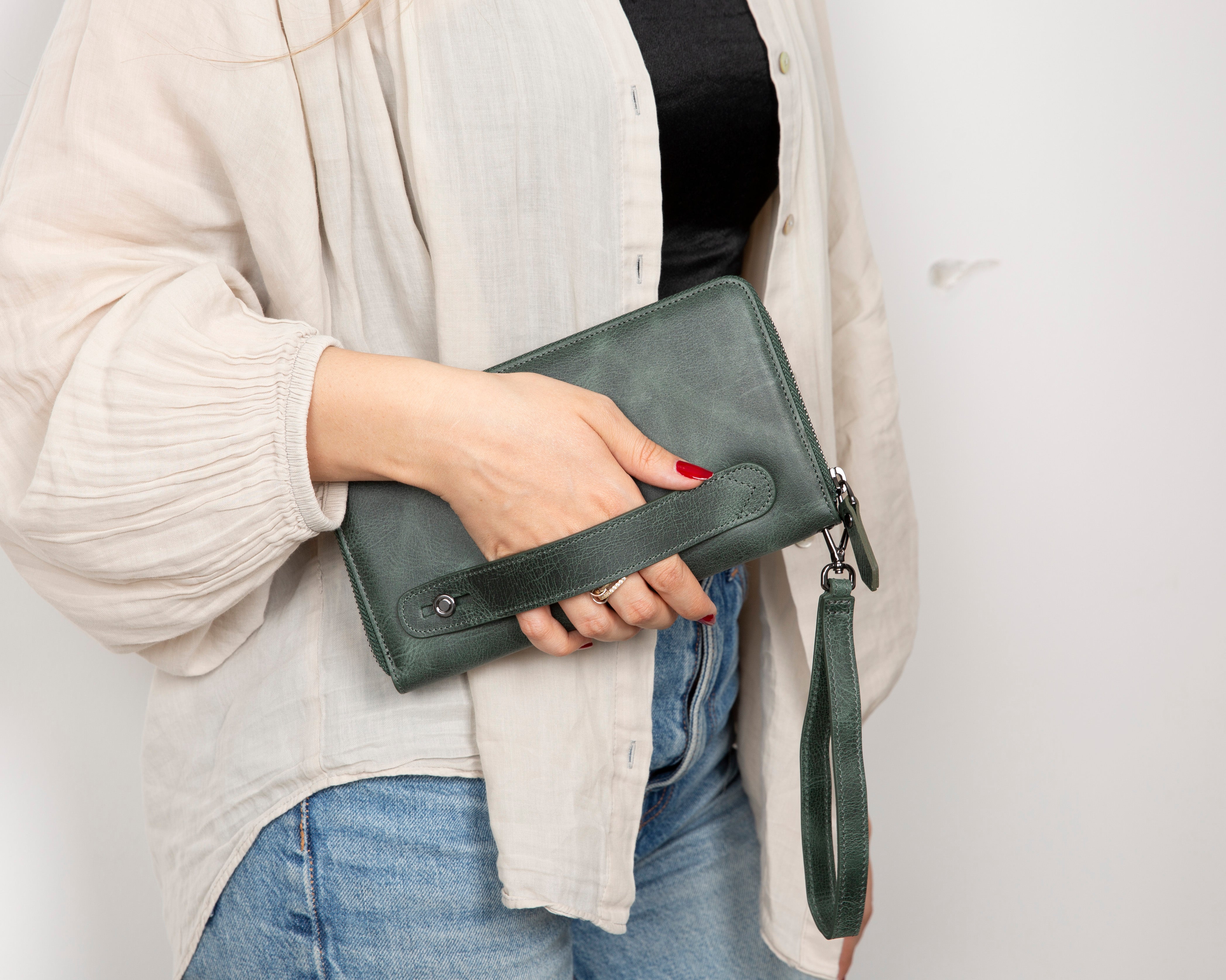 Person holding a green leather clutch bag against a plain background