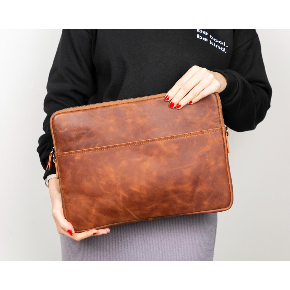 Person holding a brown leather clutch bag against a plain background