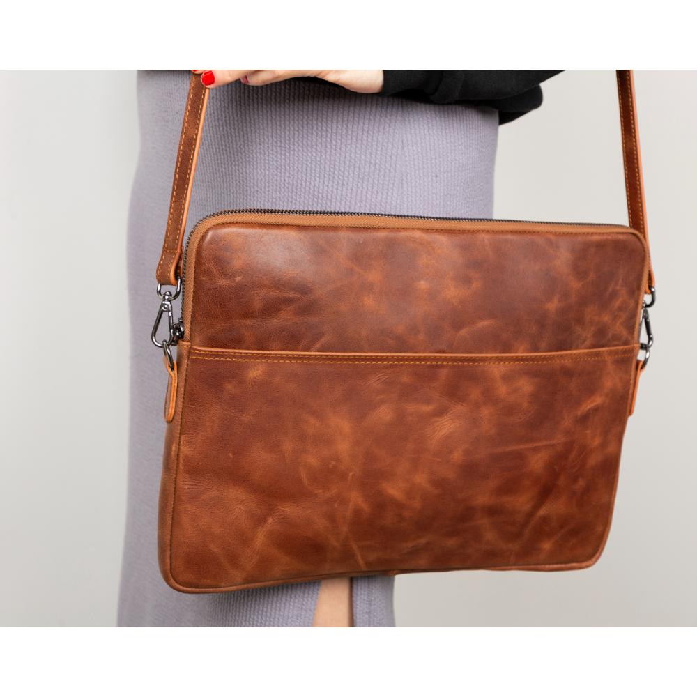 Brown leather crossbody bag held by a person on a light gray background