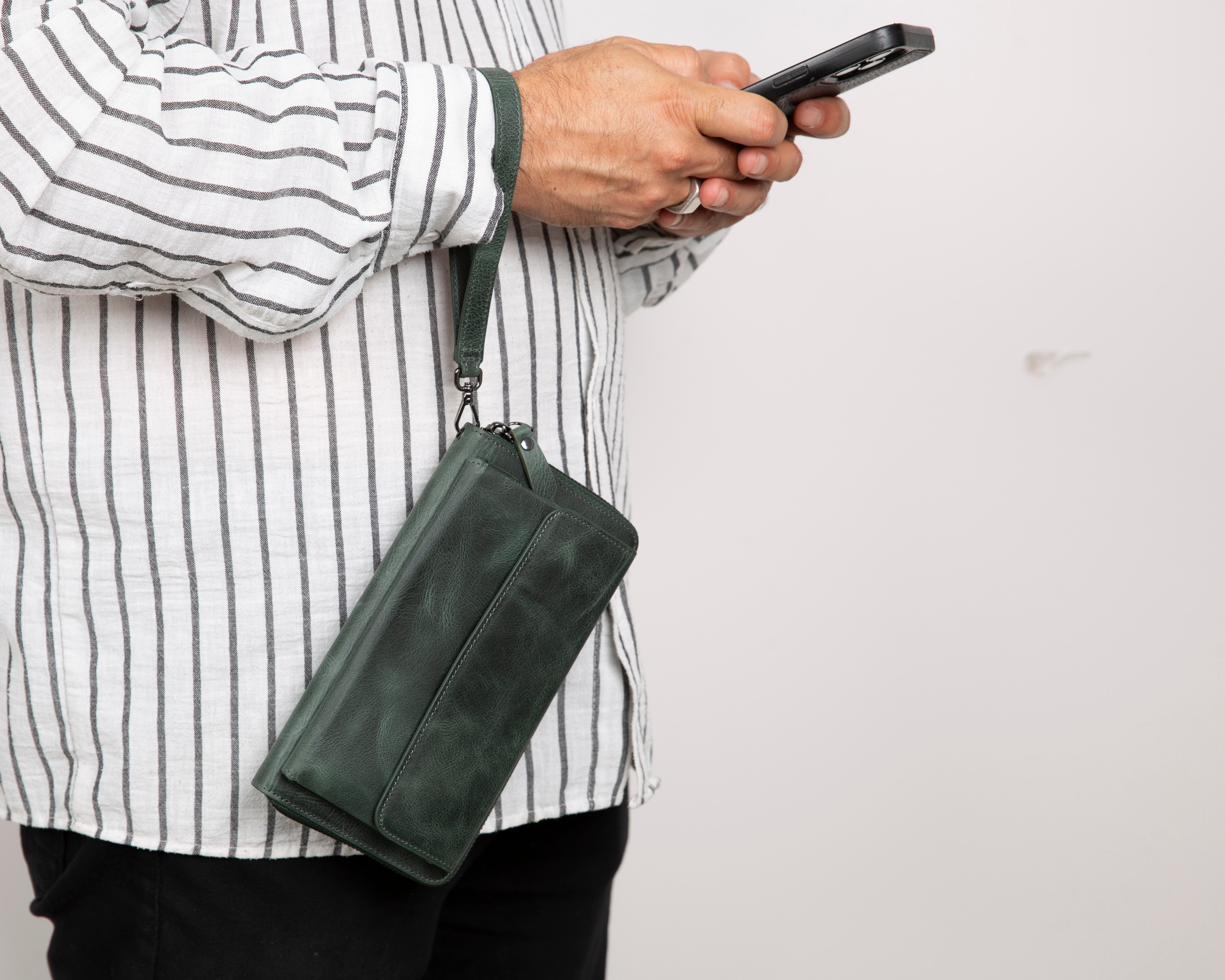 Person holding a green leather clutch bag and a smartphone against a plain background