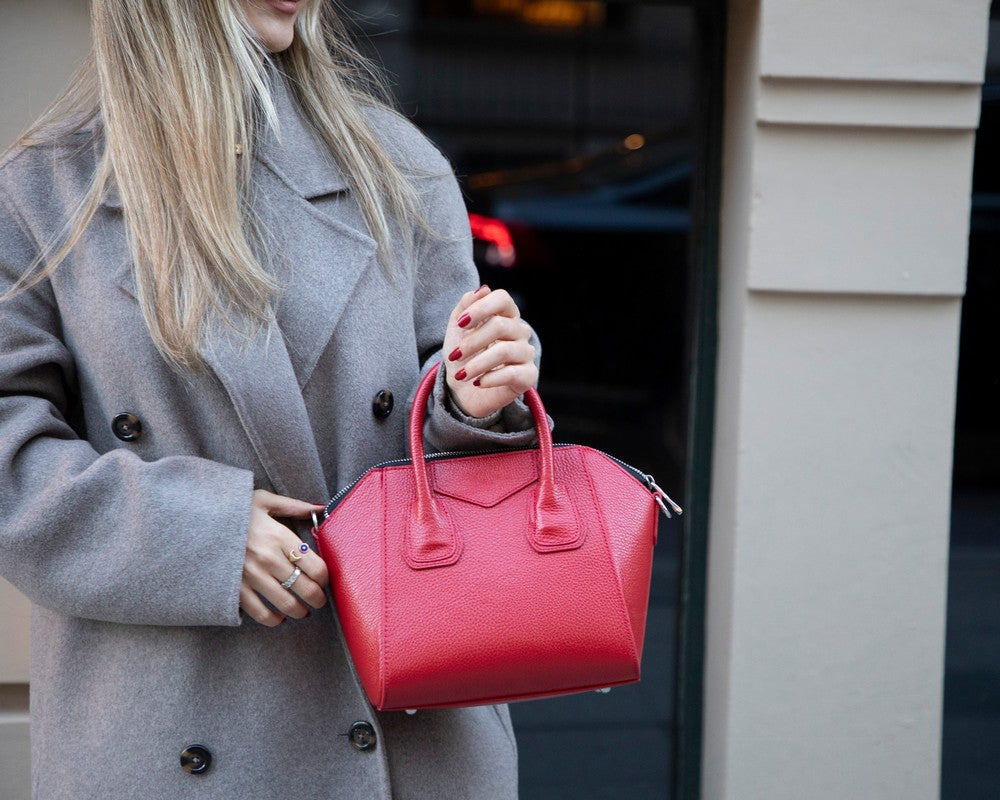 Person holding a red handbag wearing a gray coat outdoors.