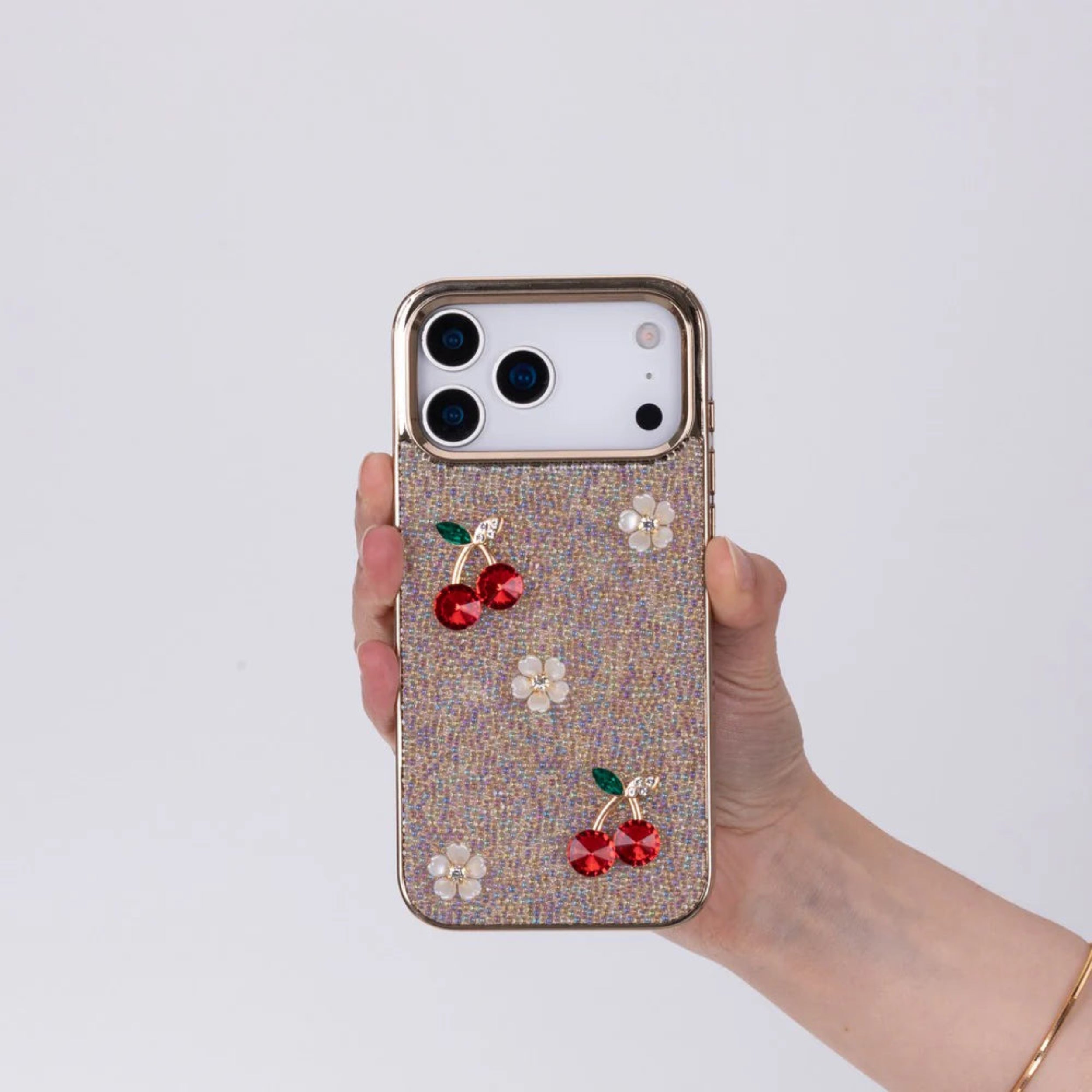 Phone case with cherry and flower designs held by a hand on a light gray background