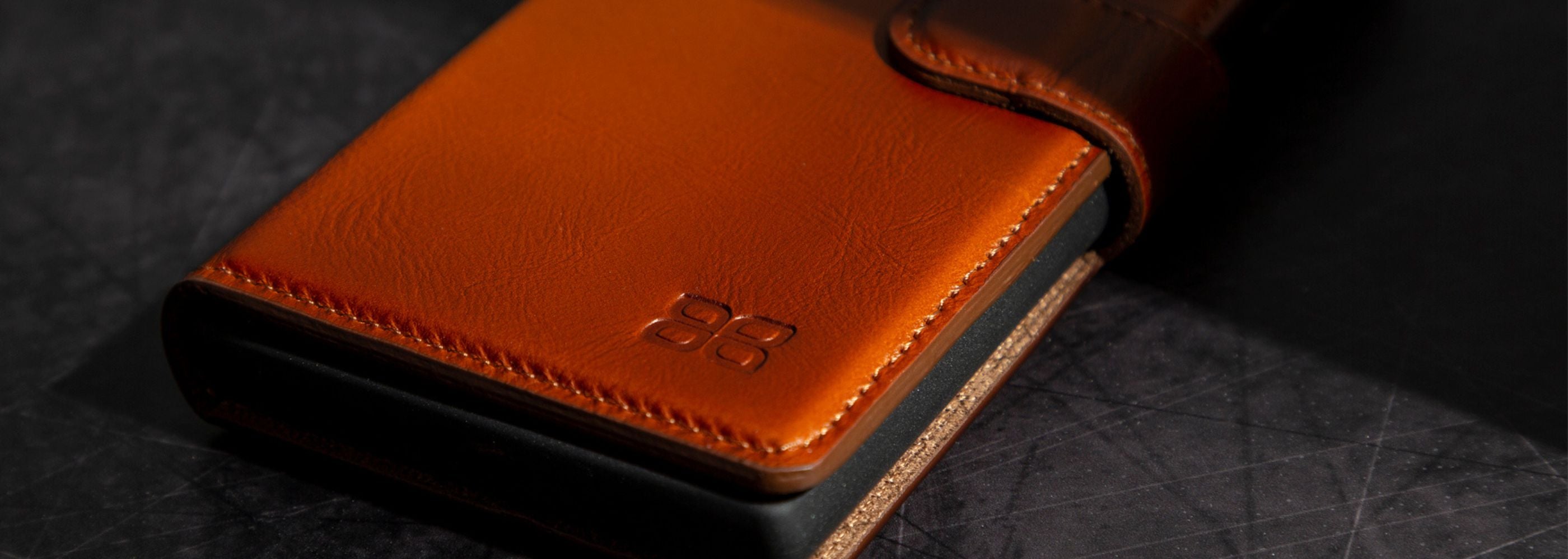Close-up of a brown leather phone case with a brand logo on a dark textured surface
