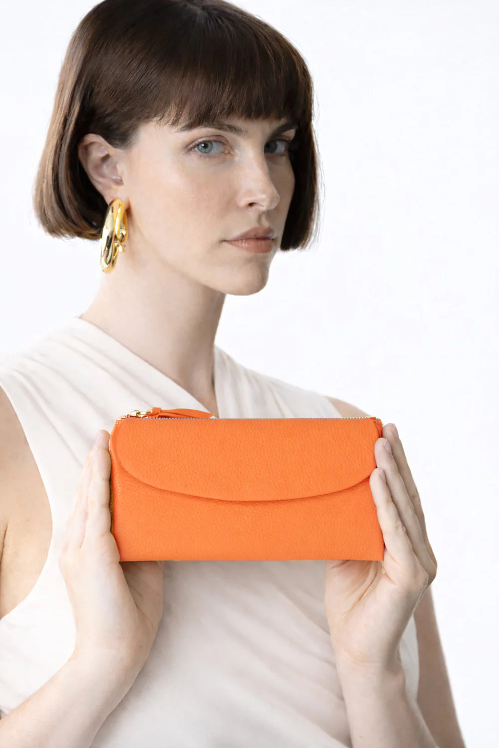 Woman holding an orange clutch against a white background