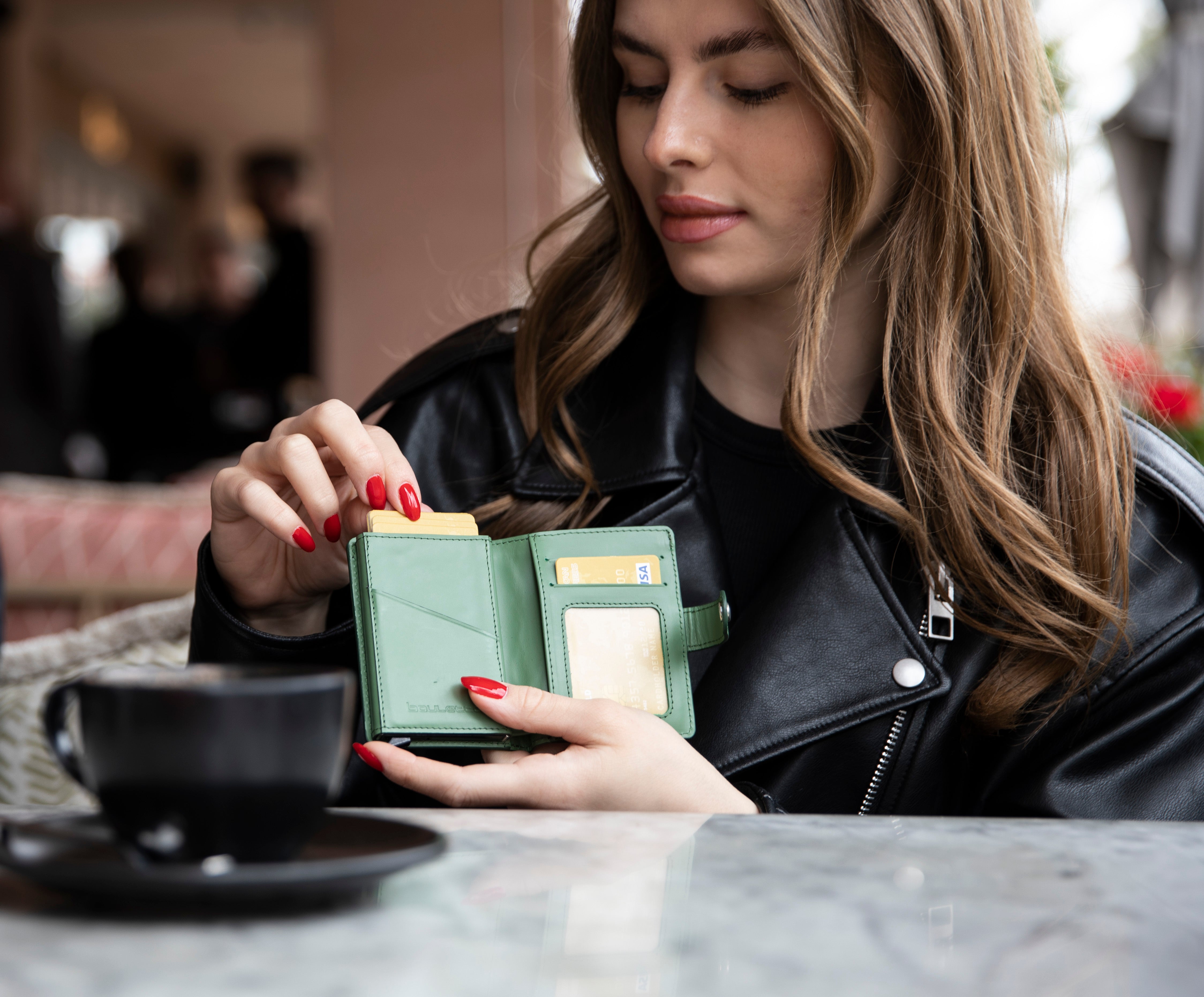 Woman taking a card from a green genuine leather wallet at a cafe table