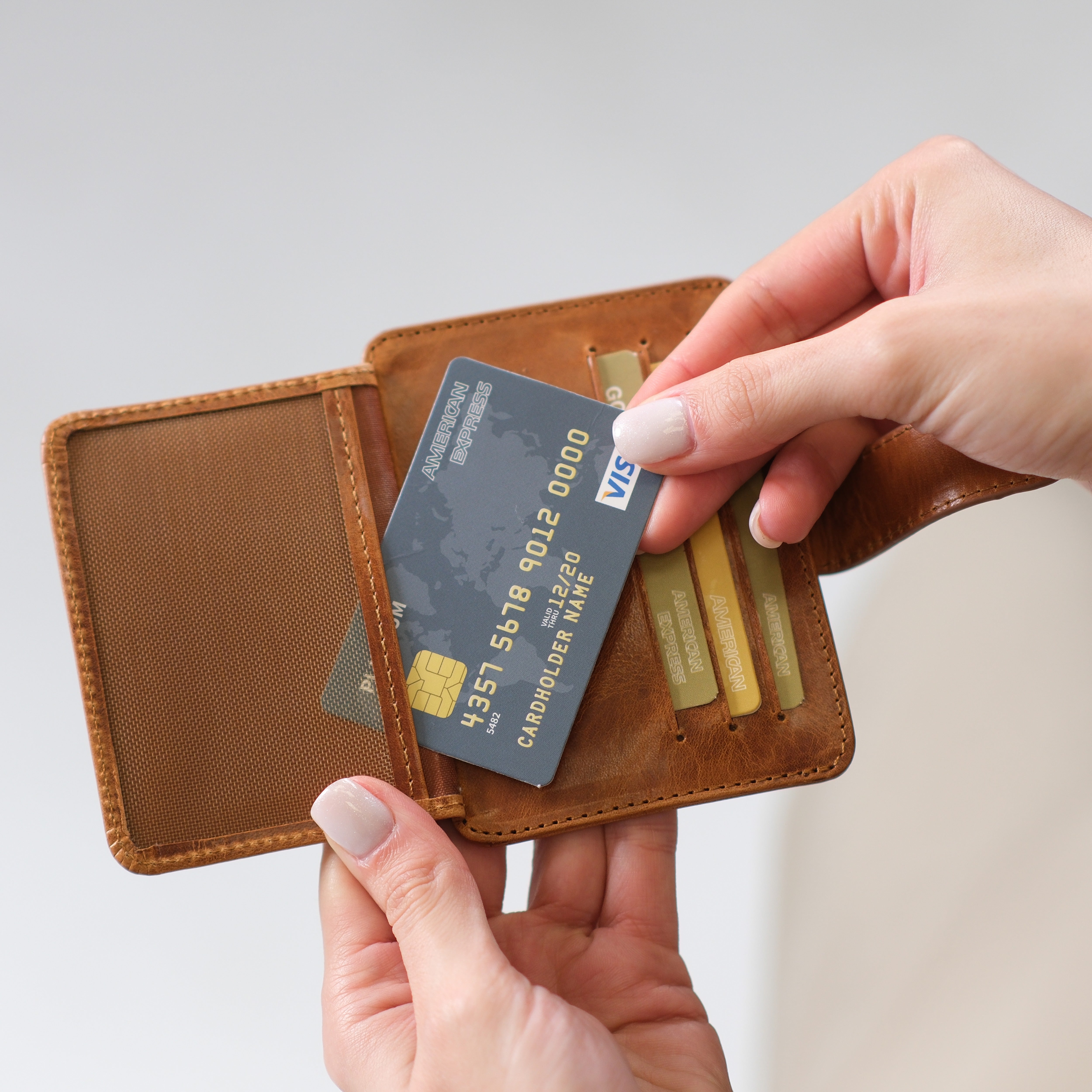 Hand placing a card into a brown leather wallet with card slots