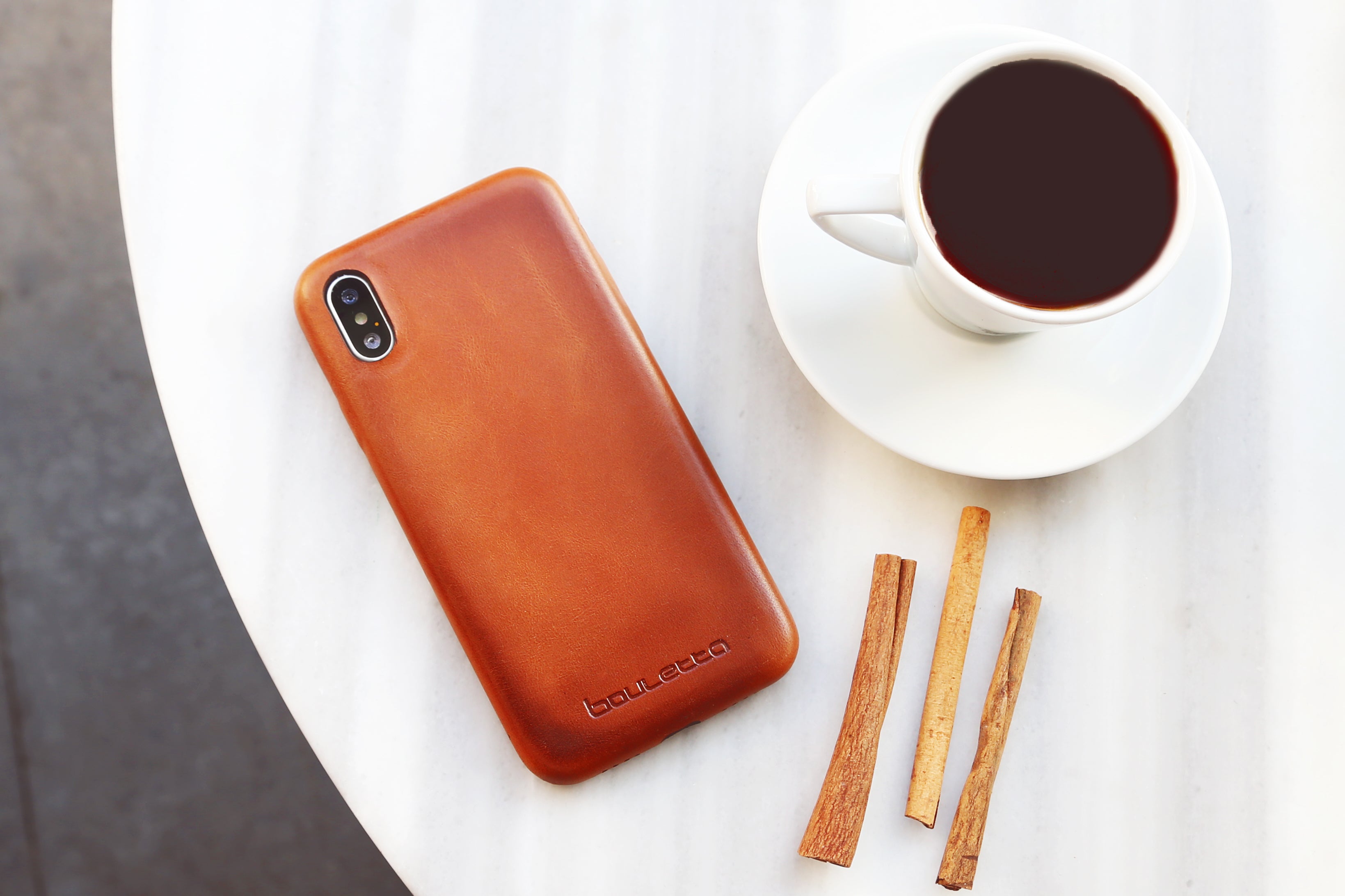 Cognac leather iPhone case beside a cup of coffee