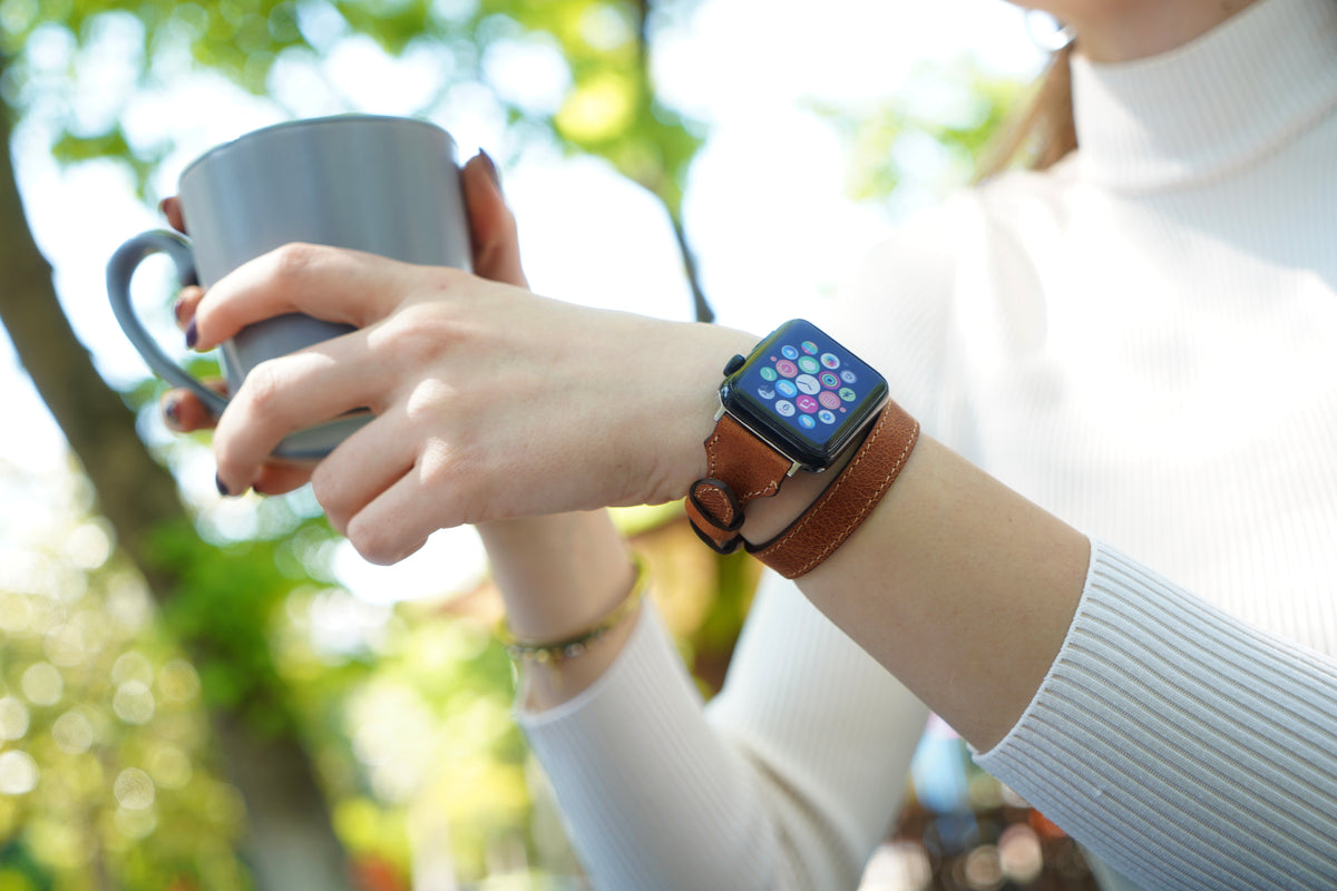 Woman wearing a brown double-tour leather Apple Watch band while holding a cup