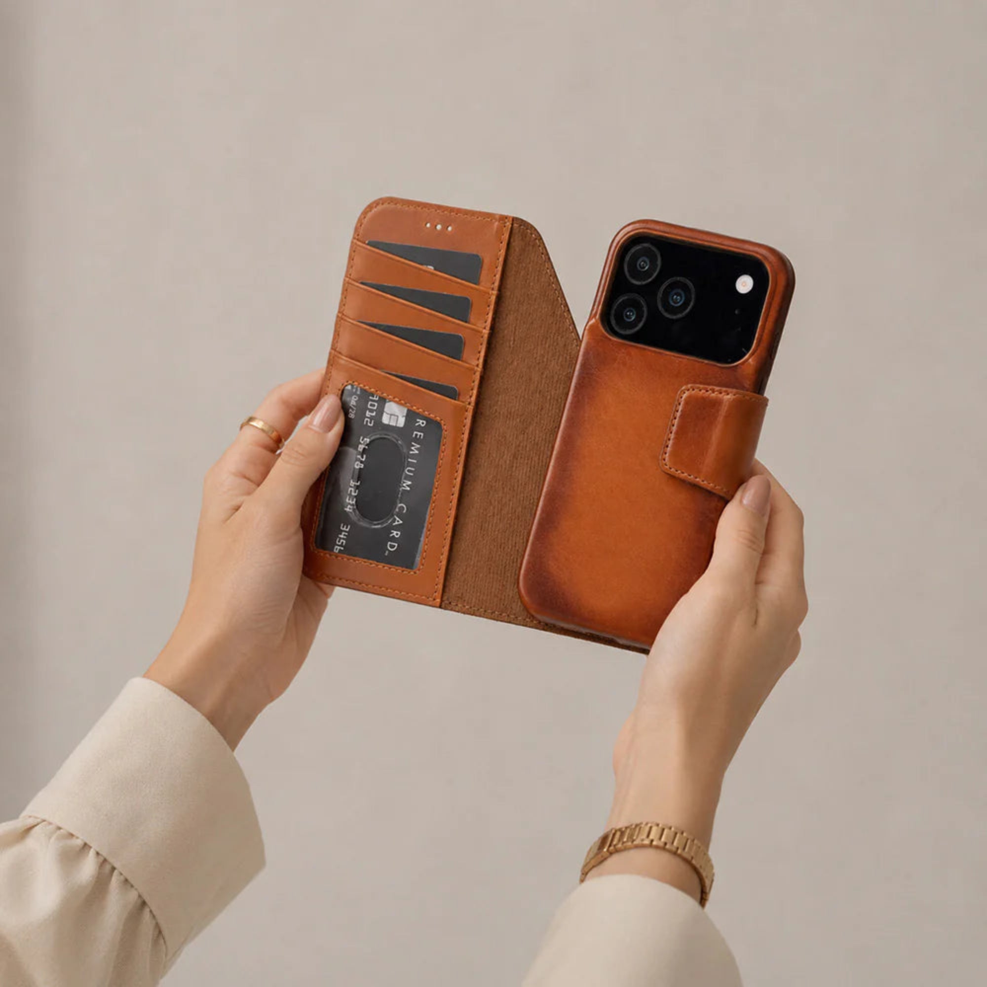 Brown leather phone case with card holder held by hands against a beige background