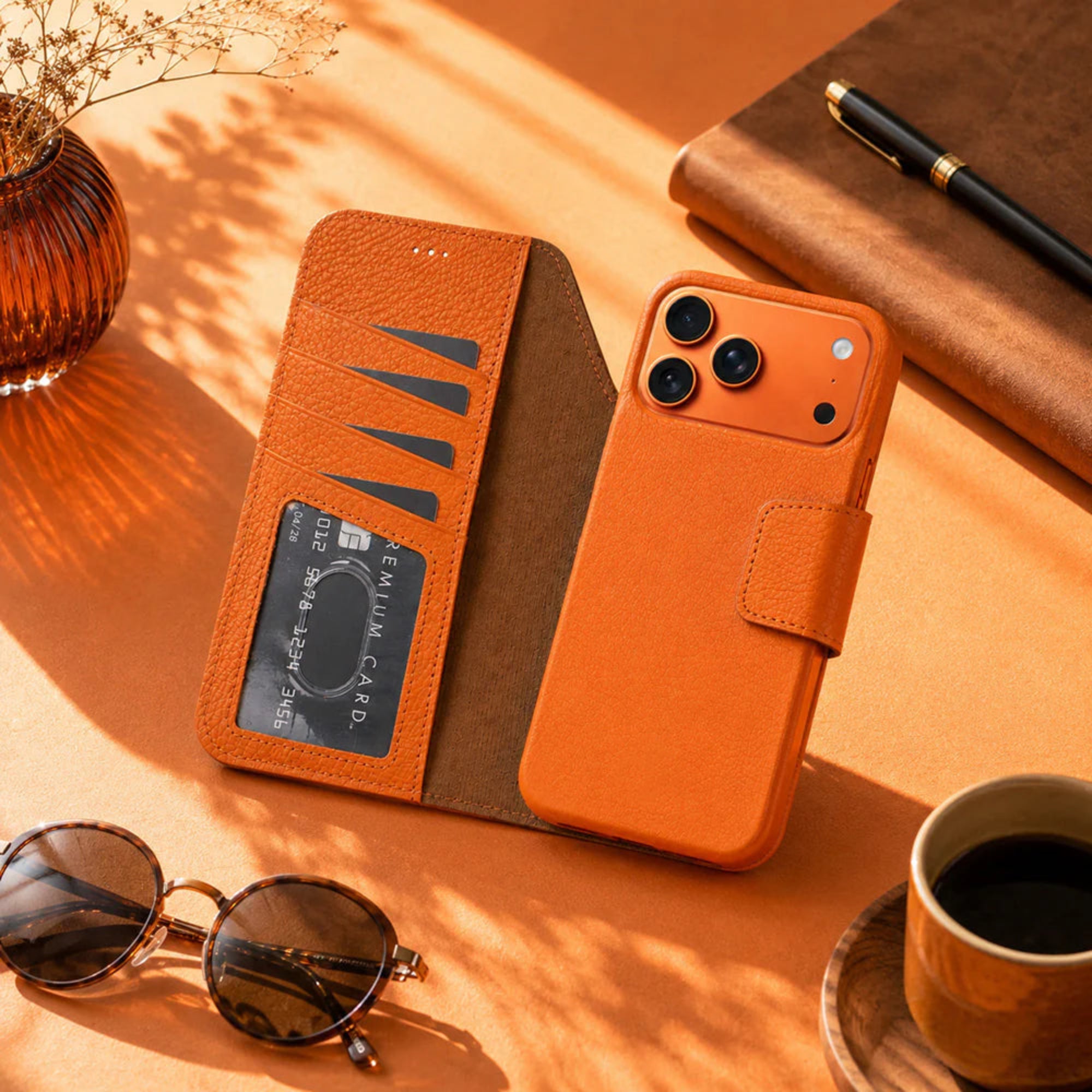 Orange phone case with card holder on a table with sunglasses, coffee, and notebook.