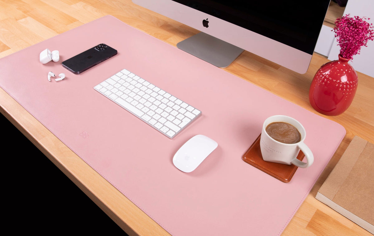 A black genuine leather desk mat displayed on a desk with a computer monitor, keyboard, mouse, and a mobile phone.