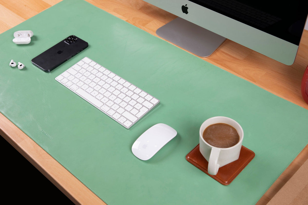 A black genuine leather desk mat displayed on a desk with a computer monitor, keyboard, mouse, and a mobile phone.