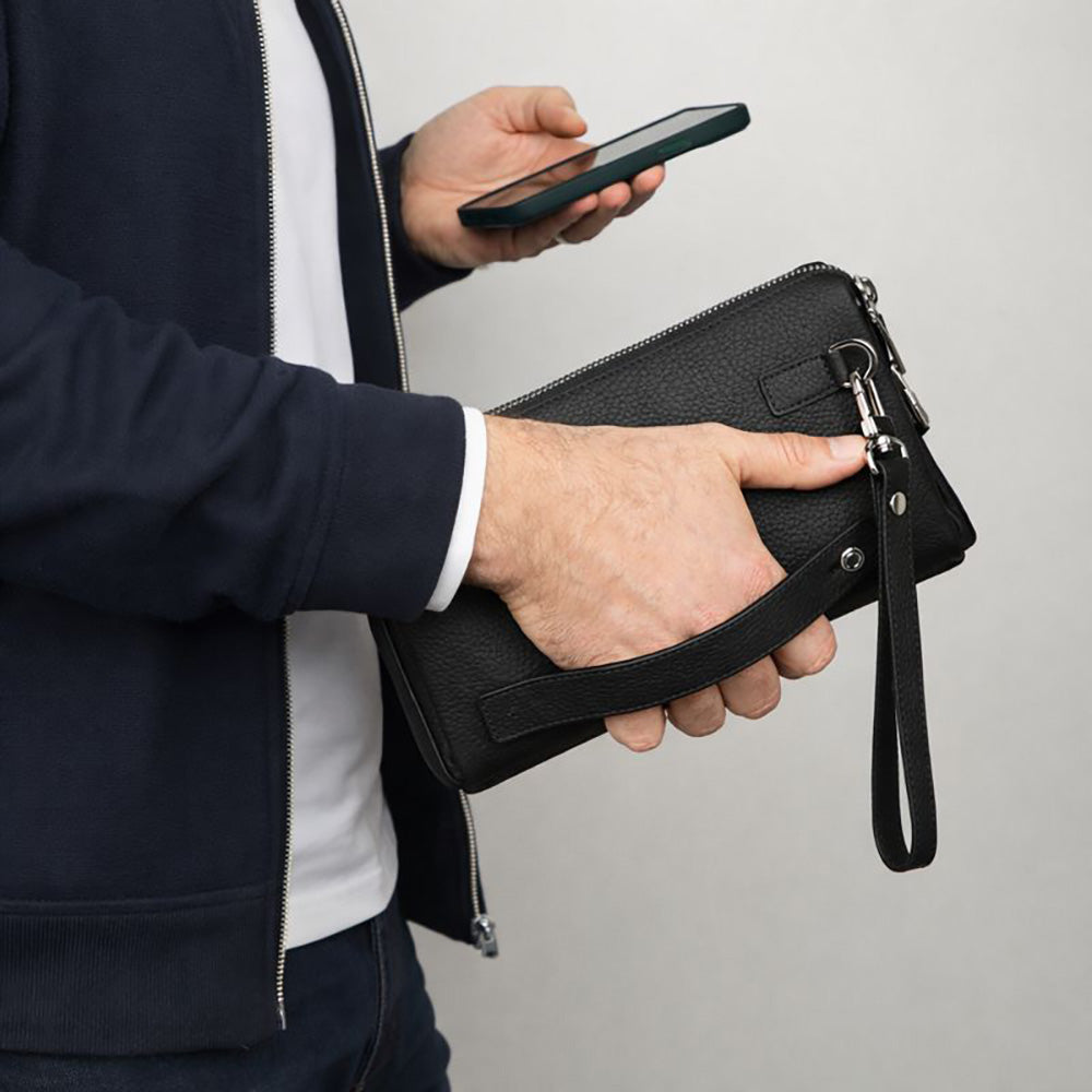 Person holding a black leather clutch bag with a plain background