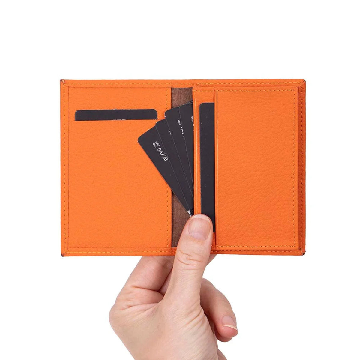 An orange textured leather bifold wallet held open by a hand, showing card slots with black cards partially inserted, against a plain white background.